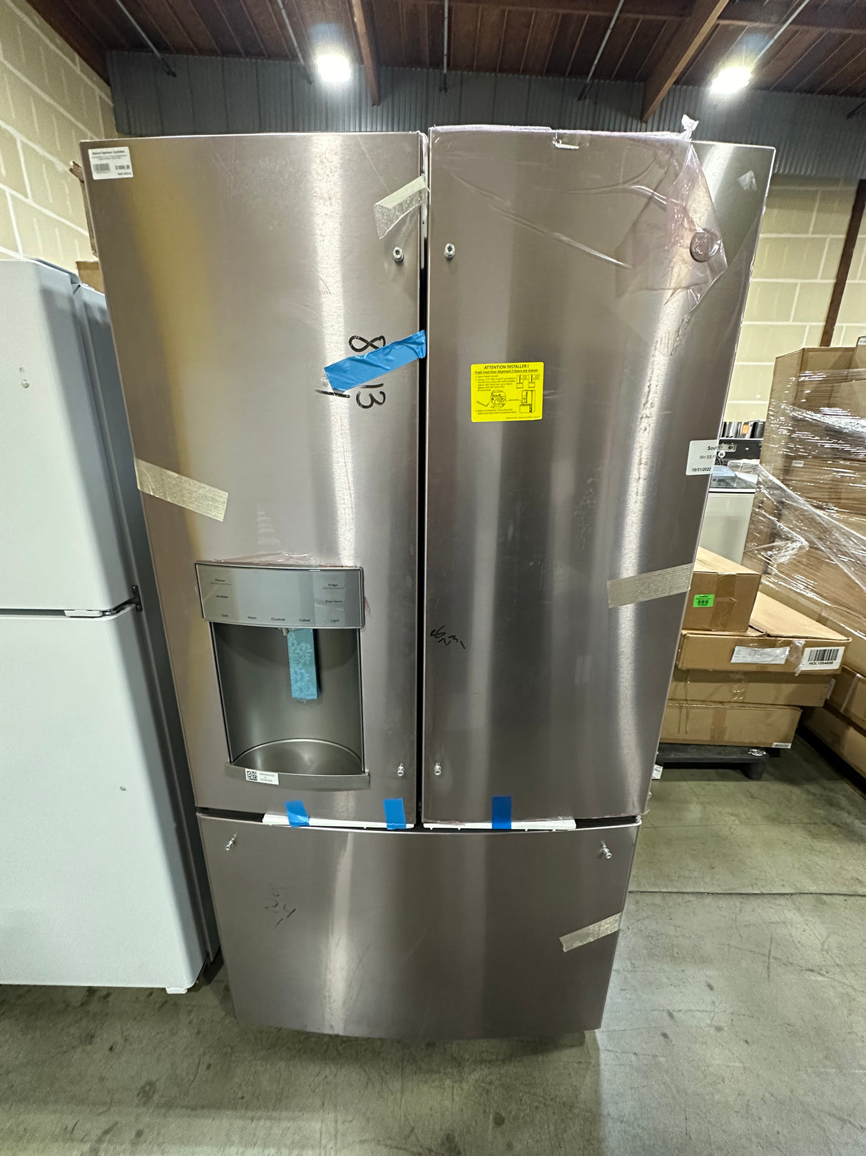 GE GFE28GYNFS 27.7 cu. ft. French Door Refrigerator in Fingerprint Resistant Stainless Steel displayed in a warehouse.
