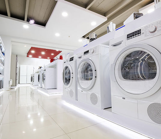 Showroom displaying various appliances like front load washers, electric dryers, and washer dryer combos on sale.